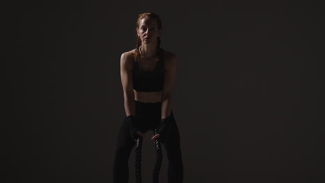 Studio-Shot-Of-Mature-Woman-Wearing-Gym-Fitness-Clothing-Doing-Cardio-Exercise-With-Battle-Ropes